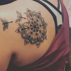 the back of a woman's shoulder with an intricate tattoo design on her left side