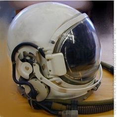 an old white helmet sitting on top of a wooden table next to a black cord