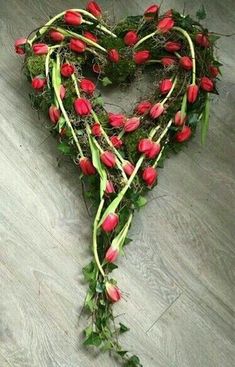 a heart - shaped arrangement of red tulips and greenery on the floor