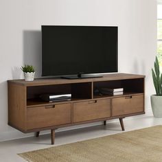 a flat screen tv sitting on top of a wooden entertainment center next to a potted plant