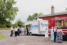 a group of people standing in front of a food truck on a gravel road next to a red building