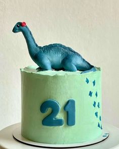 a green cake with a blue dinosaur on top and the number twenty two is displayed