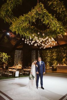 a bride and groom standing under a chandelier at their wedding reception in the evening