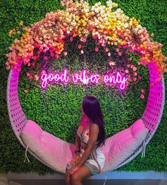 a woman sitting on a pink chair in front of a green wall that says good vibes only