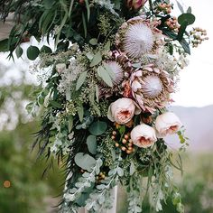 an arrangement of flowers and greenery is hanging from the ceiling in front of a building