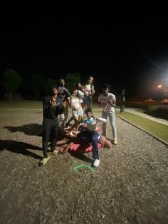 a group of people standing and sitting on top of a dirt field at night time