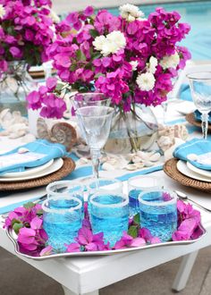 purple and white flowers are in vases next to blue glasses on a tray near a swimming pool