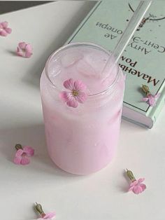 a pink drink sitting on top of a table next to a book and some flowers