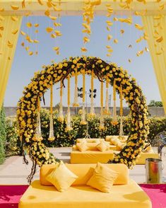 an outdoor ceremony area with yellow flowers and hanging decorations on the ceiling, along with white linen covered tables