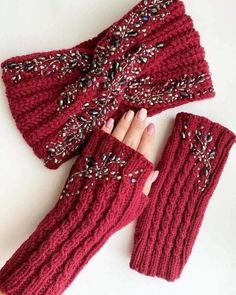 a woman's hand is holding two red knitted mittens and gloves with beading on them