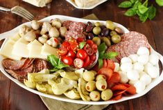 a platter filled with meats, cheese and vegetables on a table next to other foods