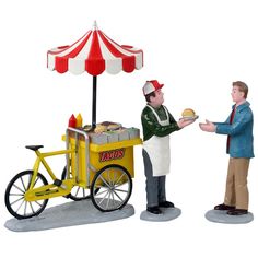 two figurines are standing next to each other near a cart with food on it