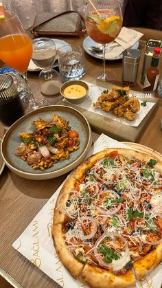 a pizza sitting on top of a wooden table next to plates of food and drinks