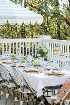 an outdoor dining table set with place settings and white umbrellas on the deck outside