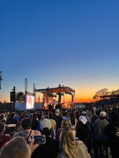 a large group of people at an outdoor concert with the sun setting in the background