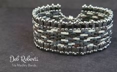 a close up of a metal bracelet on a black surface with white and gray beads