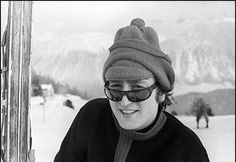 a black and white photo of a man in sunglasses wearing a beanie on skis