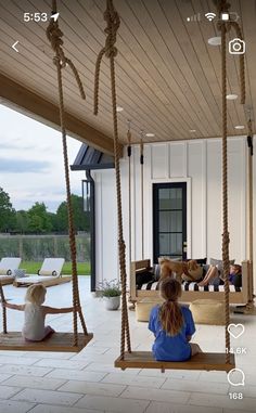 a woman sitting on a porch swing in front of a house with two people laying down