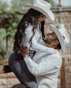 a man in a cowboy hat is holding a woman on his back while they both look into each others eyes