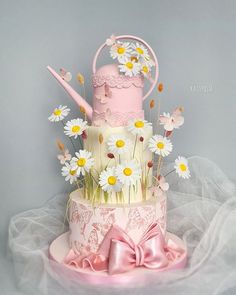 a three tiered cake decorated with daisies and pink fondant, is on display