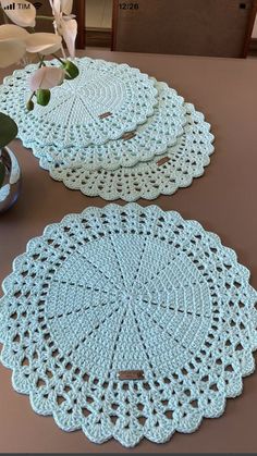 three crocheted doily sitting on top of a table next to a vase with flowers