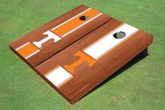 an orange and white striped cornhole board on the grass with two holes in it