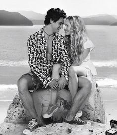 a man and woman sitting on top of a rock next to the ocean while holding each other's hands