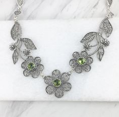 Handmade Genuine Natural Green Peridot Gemstones Sterling Silver Artisan Crafted Filigree Adjustable Statement Necklace Material: 925 Solid Sterling Silver, 925 Stamped Natural Peridot Gemstones: 6 mm each, Round, Faceted Necklace Length: 19 inches Center Flower Length: 1 inch Width: 1 inch Closure: Lobster claw clasp Comes with a gift box Free Domestic Shipping It is a gift that will create memories for years to come. Filigree is the art of embroidery with metal thread. Our aim is to exceed all Floral Statement Necklace, Filigree Necklaces, Silver Jewelry Design, August Birthstone, Sterling Silver Filigree, Peridot Gemstone, Green Peridot, Necklace Women, August Birth Stone