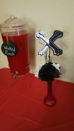 a red table topped with a vase filled with flowers next to a black and white sign