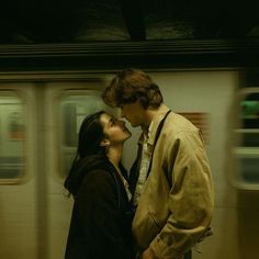 a man and woman standing next to each other in front of a subway train at night