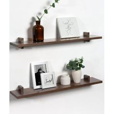 two wooden shelves with pictures and vases on them, one has a plant in it