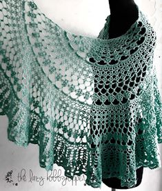 a green crocheted shawl draped over a mannequin