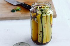 a jar filled with pickles sitting on top of a table next to a knife