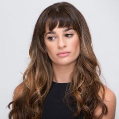 a woman with long brown hair and bangs looking at the camera while wearing a black top