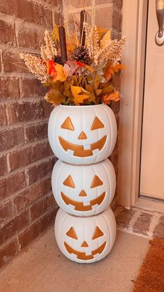 three pumpkins stacked on top of each other in front of a brick wall and door