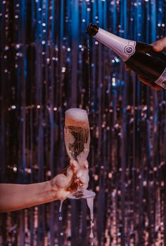 a person pouring champagne into a wine glass in front of a wall with streamers