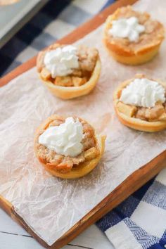 mini apple pies with whipped cream on top sitting on a cutting board, ready to be eaten