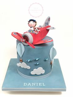 a cake that is shaped like a plane with a boy on top and clouds around it