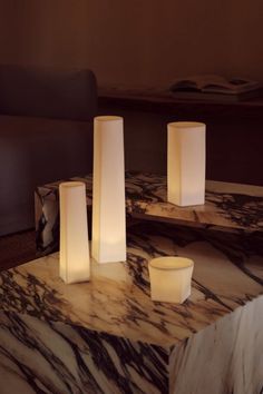 three white candles sitting on top of a marble table next to a couch in a living room