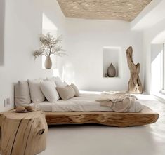 a large bed sitting on top of a white floor next to a wooden table and vase