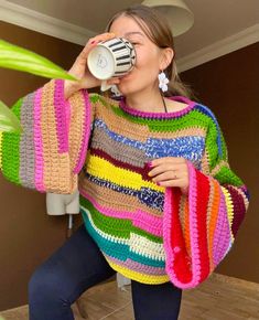 a woman drinking from a cup while wearing a colorful sweater