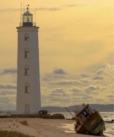 a small boat sitting on top of a beach next to a light house in the ocean