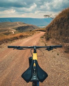 a bike parked on the side of a dirt road near a grassy field and mountains