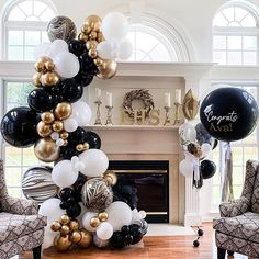 black, white and gold balloons are hanging in front of a fireplace