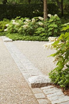 a white umbrella sitting on top of a stone walkway next to flowers and trees in the background