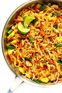 a pan full of noodles and vegetables with limes on the side for garnish