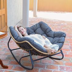 a woman is sleeping in a chair on the brick floor next to a table and door