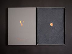 an open book with a gold letter on the front and back cover, sitting on a black surface