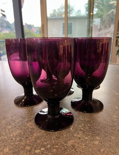 three purple wine glasses sitting on top of a counter