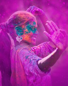 a woman covered in purple and blue powder holding her hands out to the side,